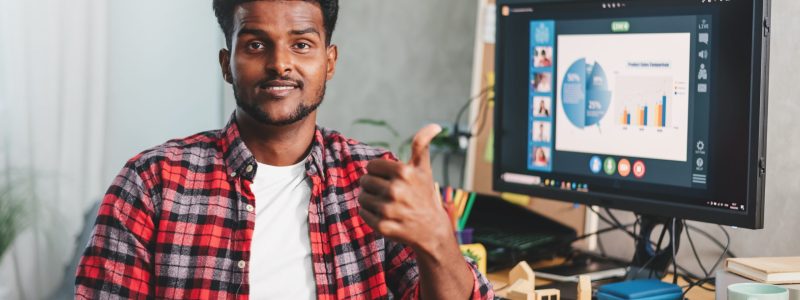 African american young man work at home, showing thumb up for good work on the background of working desk.